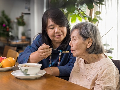 a woman helps an older woman eat her soup