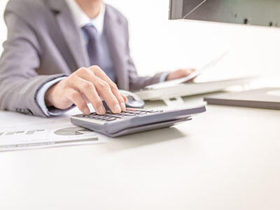 Man in a suit sitting at a computer and using a calculator.